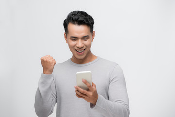 Happy excited Asian man looking at his smartphone and raising his arm up to celebrate success