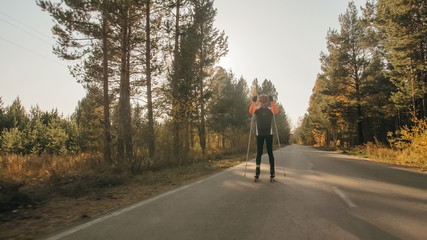 Training an athlete on the roller skaters. Biathlon ride on the roller skis with ski poles, in the helmet. Autumn workout. Roller sport. Adult man riding on skates.