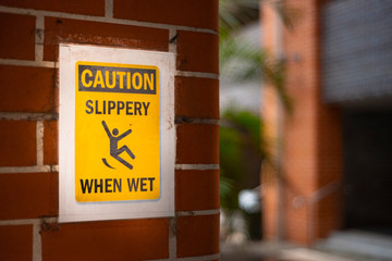 Square Yellow caution sign slippery when wet on the red brick wall.