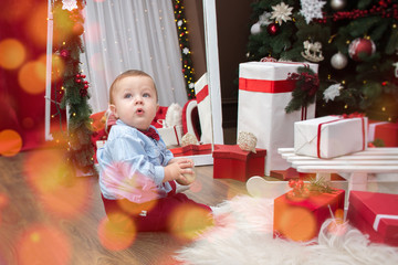 Fototapeta na wymiar little boy plays with presents in a room decorated on the eve of Christmas
