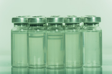 Glass medical ampoule vial for injection. Medicine is liquid sodium chloride with of aqueous solution in ampulla. Close up. Bottles ampule multicolor on background color and water. Human plasma.