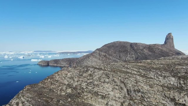 Slow ascending drone view of the rocky terrain of Kullorsuaq, Greenland, coasting the deep blue arctic sea, showing high details of the ground surface and icebergs that float in the Baffin sea