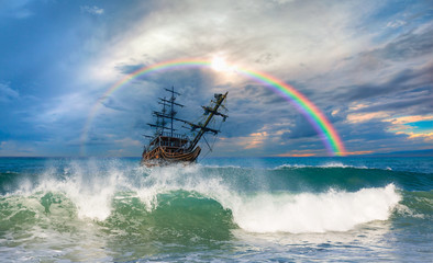 Old ship sailing at the sea under the rainbow and blue sky 