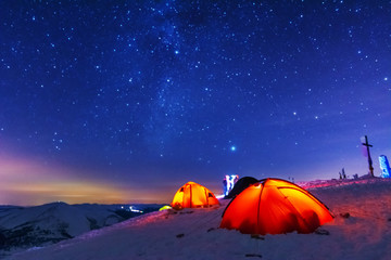 Great bright campsite with colorful tourist tents, on top in the Ukrainian Carpathian Mountains, at night with views of the stars and the Milky Way	