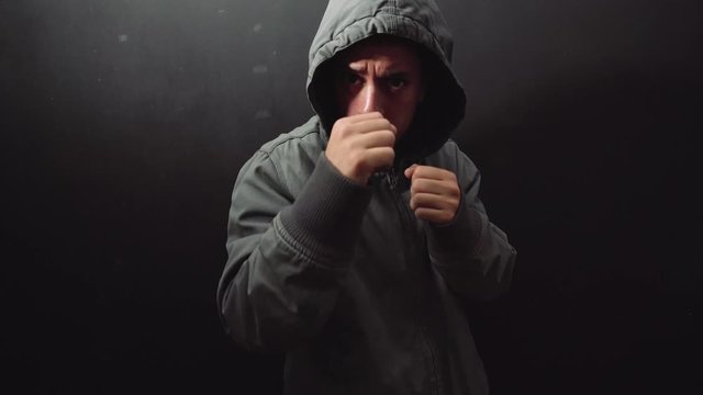 man with hood fighting in a black background