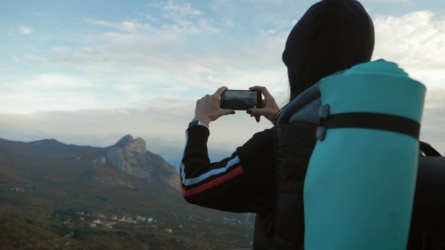 Girl on mountain top, female tourist taking photo of on cell smart phone. Young woman traveler on a background of mountains takes photos on a mobile phone.