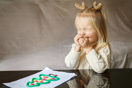 Adorable little girl with blonde hair playing with clay and making christmas tree at home