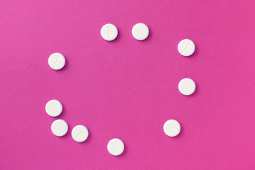 White round pills tablets on a bright pink background close up. Top view, copy space. Medical concept