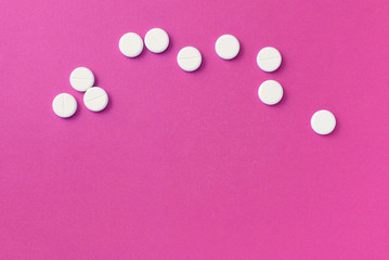 White round pills tablets on a bright pink background close up. Top view, copy space. Medical concept