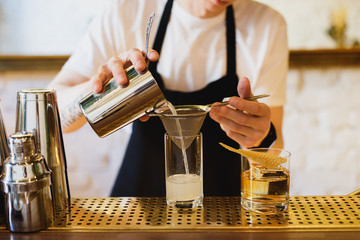 Pouring a drink from a shaker through a strainer into a highball glass. Selective focus. Horizontal lifestyle image.