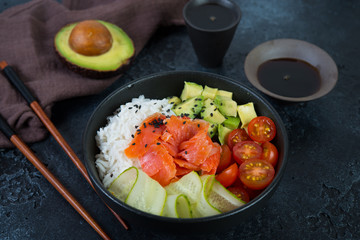 A popular Hawaiian dish, Poke in a plate of red fish, rice and vegetables. Poke plate on a black concrete background