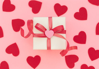 White gift box with red ribbon and pink heart on pink background with lots of red hearts. Valentine's Day concept. Valentine greeting card. Flat lay style.