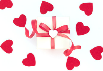 White gift box with red ribbon and white heart on white background with lots of red hearts. Valentine's Day concept. Valentine greeting card. Flat lay style.