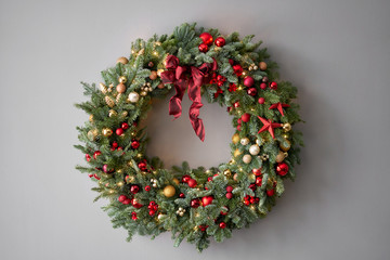 Beautiful festive wreath of fresh spruce on Gray wall. Xmas circlet with red and gold ornaments and balls. Christmas mood.