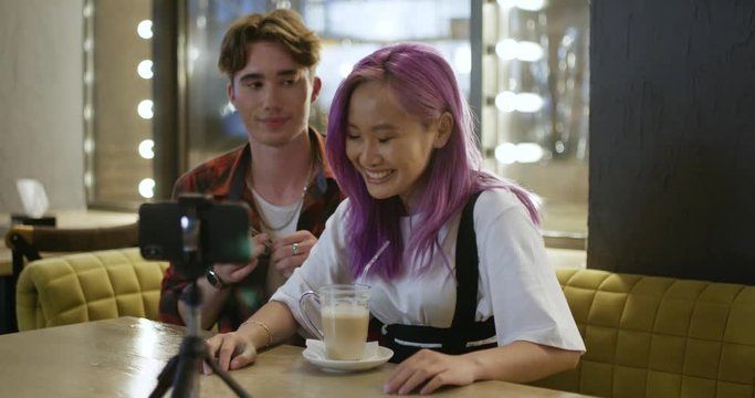 Young couple in cafe, guy and girl communicate and record a video blog on smartphone, positive emotions, blurry lights on background, 4k.