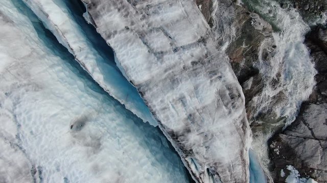 Stationary aerial drone top view over the glacier of Sam Ford Fjord, Canada, near Greenland, showing ice melting from the glacier and a water stream of the nearby river