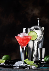 Red Watermelon alcoholic cocktail with vodka, juice, lime and crushed ice, metal bar tools, dark background