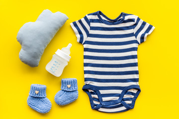 Blue bodysuit for baby boy near children's accessories on yellow background top-down