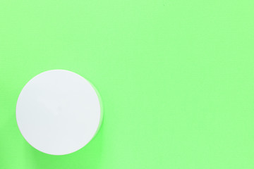White cosmetic jar on a green background close up. Top view, copy space
