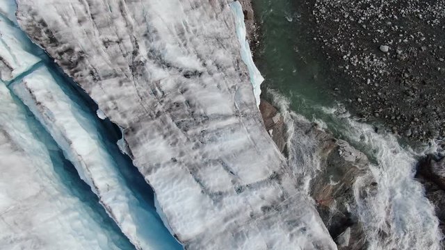 Aerial drone tilt view of the glacier of Sam Ford Fjord, Canada, near Greenland, showing ice melting from the glacier and a water stream of the nearby river flowing in the arctic sea
