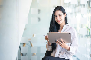 Young Asian graphic designer working on graphics tablet in her working space. Young college students reading somthing from her tablet.