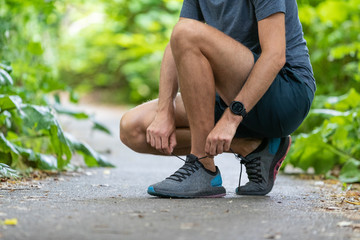 Running fit man tying shoes wearing wearable technology smart watch. Fitness runner athlete getting...