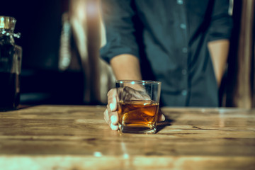 Hands of a bartender, with a glass of whiskey, soft focus.