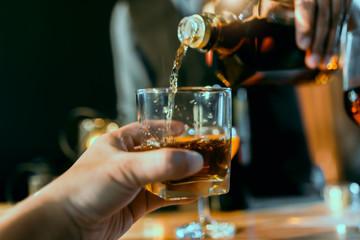 Hands of a bartender, with a glass of whiskey, soft focus.