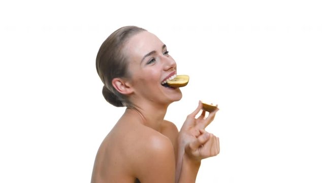 Piękna wesoła modelka ze zdrową sk&oacute;rą pozuje z owocem kiwi. Koncepcja zdrowego żywienia oraz dbania o urodę i zdrowie. Na białym studyjnym tle.