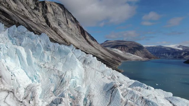Slow aerial drone ride over the glacier of Sam Ford Fjord, Canada, near Greenland, revealing high details of natural ice and rocks with harsh and strange relief, on a sunny day