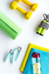 Fitness background - dumbbells, jump rope, sport carpet, water bottle - on white top-down