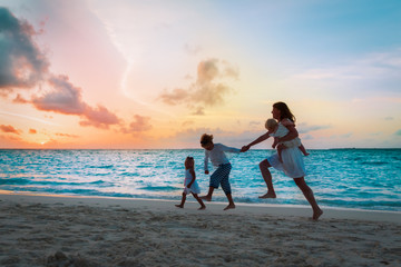 mother with kids run and play on beach at sunset