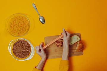 Woman on diet holds measuring tape with buckwheat and macaroni products in the glass plates around. Slow carbohydrates on the orange background with copy space.