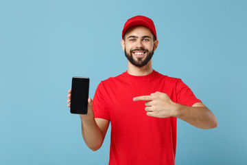 Delivery man in red uniform workwear hold cellphone isolated on blue background, studio portrait. Professional male employee in cap t-shirt working courier dealer. Service concept. Mock up copy space.