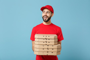Delivery man in red workwear giving food order pizza boxes isolated on blue background, studio...