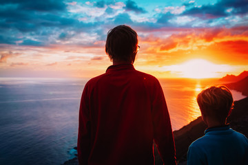father and son looking at sunset at sea while travel in mountains