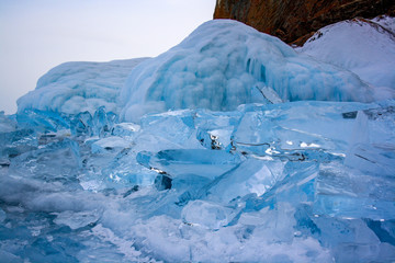 A pile of broken transparent ice near a cliff on Lake Baikal. Beautiful blue color of ice. On the rock is red moss.