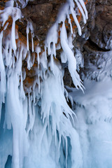 Icicles melted in the sun and bent from the wind on a rock. Smooth ice. Cloudy weather. Vertical.