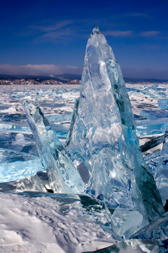 Naklejki A large broken transparent piece of ice stands frozen vertically on Lake Baikal. A lot of broken ice around. Beautiful blue and green color of ice. Vertical.