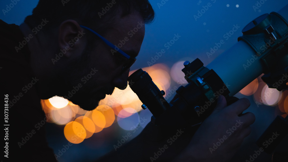 Wall mural astronomer with a telescope watching at the stars and moon with blurred city lights in the backgroun