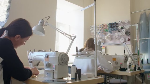 Two women seamstresses working on sewing machines in the tailoring workshop of the garment. The creation of designer dresses. Small business. Two employees work on sewing machines from the back.