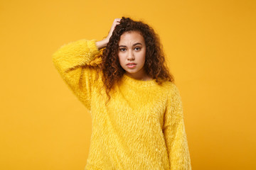 Preoccupied young african american girl in fur sweater posing isolated on yellow orange background studio portrait. People sincere emotions lifestyle concept. Mock up copy space. Putting hand on head.