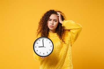 Preoccupied young african american girl in fur sweater posing isolated on yellow orange background,...