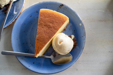 Flatlay view of cheesecake and vanilla ice cream a la mode on a blue plate with spoon