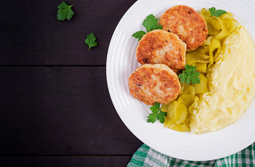 Homemade fried cutlets/meatballs with mashed potatoes and pickled cucumber on white plate. Top view, overhead, copy space.