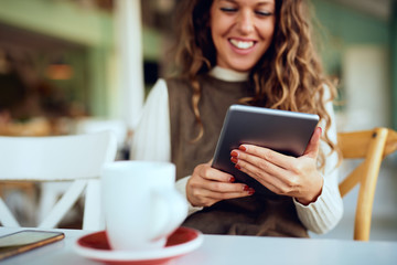 Attractive young curly brunette enjoying her coffee/tea and working on tablet