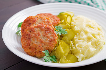 Homemade fried cutlets/meatballs with mashed potatoes and pickled cucumber on white plate.