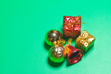 Top view of Christmas gift box red balls with spruce branches and bell on green background.