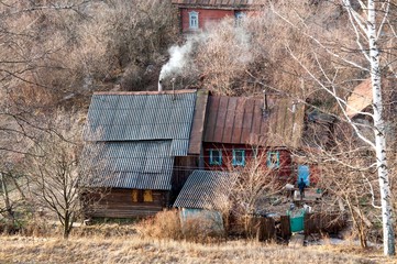 an old abandoned house in the village in the autumn in a forest overgrown with trees with a Smoking chimney from the furnace