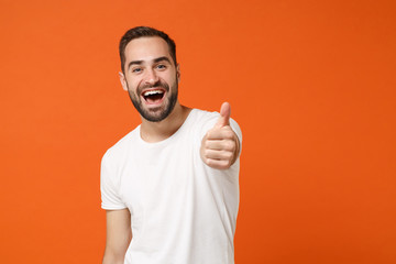 Fototapeta premium Excited funny young man in casual white t-shirt posing isolated on bright orange wall background, studio portrait. People sincere emotions lifestyle concept. Mock up copy space. Showing thumb up.